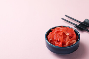 Bowl with red pickled ginger and chopsticks on pink background