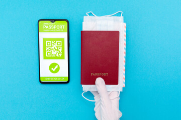 A hand in protective glove holds a passport with mask and ticket. Cellphone screen with an electronic health passport with qr-code. Flat lay. Concept of Covid-19 test for travel