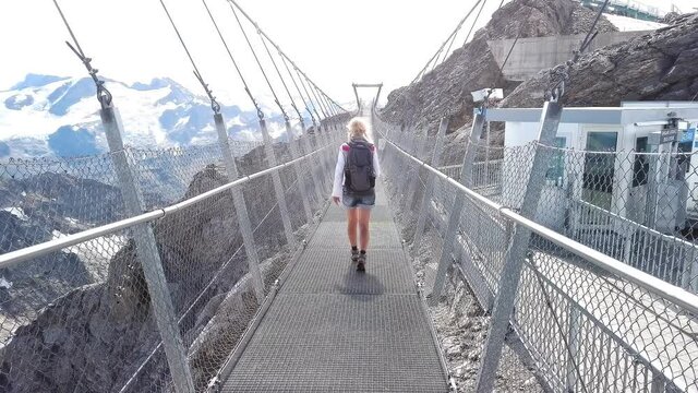 Titlis cliff walk suspension bridge on top of Titlis mountain with glacier in the Uri Alps. Viewpoint 3028 m located in cantons of Obwalden and Bern, Switzerland, Europe. Summer season blue cloudy sky