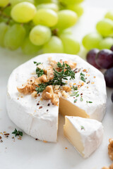 Brie or camembert cheese with walnuts, thyme and grapes. Slice of soft white camembert cheese cut out