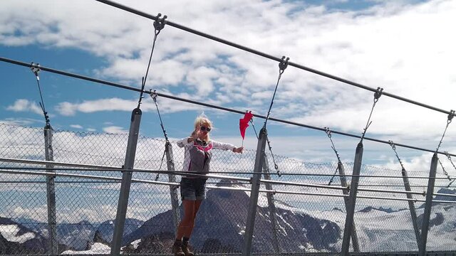Swiss Woman on suspension bridge waving flag of Switzerland. Titlis cliff walk in the Uri Alps. Viewpoint at 3028 meters in Summer season, Bern canton. The highest suspension bridge in Europe.