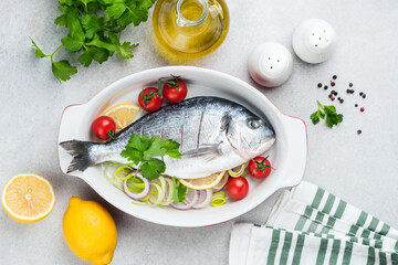 Uncooked Dorado fish with vegetables in ceramic dish ready for cooking