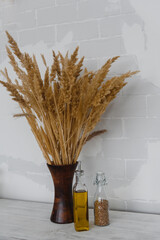 a vase of dried plants and bottles of oil against a light brick wall