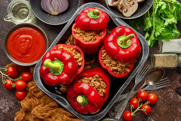 Red bell stuffed paprika peppers in iron cooking pot with various ingredients on side