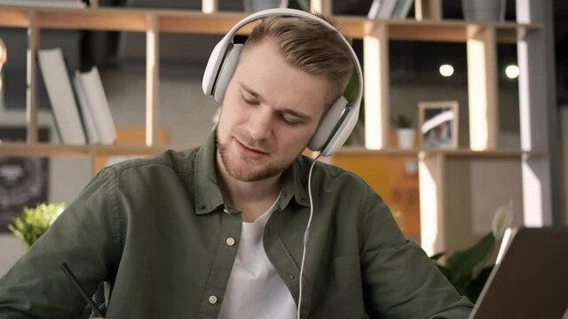 Businessman or male freelancer working from home office. Serious man makes notes in notebook sheets in living room. Learning courses and online education. Student talking online video chat conference