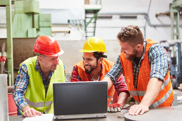 Workers in factory together in front of laptop computer