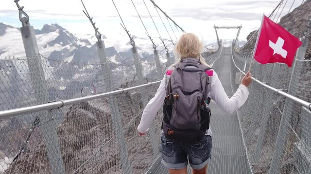 SLOW MOTION: Woman with Swiss flag on Titlis suspension bridge. Top of Titlis mountain with glacier in the Uri Alps. Viewpoint 3028m in cantons of Obwalden and Bern, Switzerland, Europe. Summer season