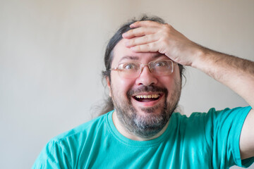 Obraz premium Close-up of an adult man with long hair. A man in glasses with a smile and surprise holds his head