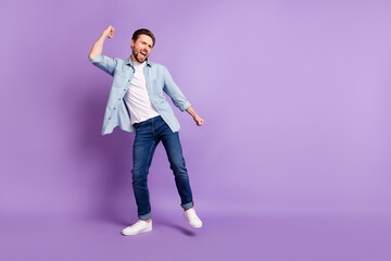 Photo of funky charming young man wear jeans shirt dancing smiling empty space isolated violet color background