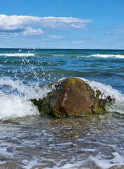 Welle bricht sich an einem Findling in der Ostsee