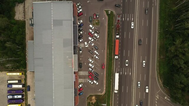 Top view aerial shot - a section of the highway near the supermarket with parking cars and buses at summer day. Traffic on the suburban highway near the shopping center with parking - top view shot