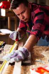 Woodworker measuring wooden plank. Young male carpenter working in workshop..