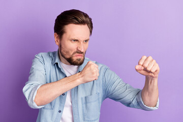 Photo of unhappy mad furious young man look empty space raise fists fight isolated on violet color background
