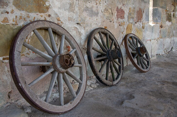 Fototapeta na wymiar Three old wooden wagon wheels stand in front of a sandstone wall