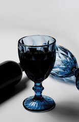 A bottle of red wine with a blue wine glass, on a white background