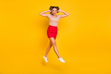 Fototapeta na wymiar Full length body size view of pretty cheerful girl jumping having fun showing v-sign near eye isolated on bright yellow color background