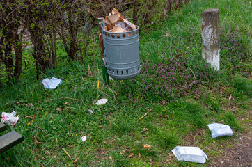 Fototapeta premium Public garbage bin swells, packaging waste lies next to it