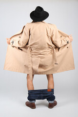 Exhibitionist exposing naked body under coat on light background, back view