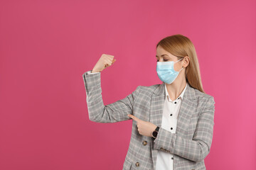 Businesswoman with protective mask showing muscles on pink background, space for text. Strong immunity concept