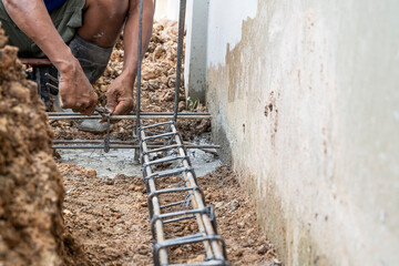 Hands of the workers are binding the wire with steel bars at the construction site - obrazy, fototapety, plakaty