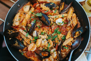 Classic dish of Spain, seafood paella in traditional pan on rustic wooden background top view. Spanish paella with shrimps, clamps, mussels, green peas and fresh lemon wedges from above