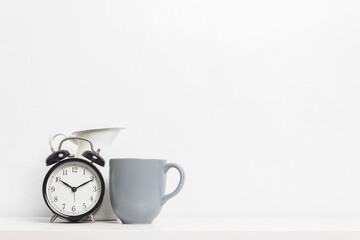 An alarm clock and cup of coffee with white jar on table.