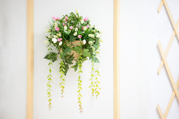 A flower pots with leaves and flowers hanging on a white wall.