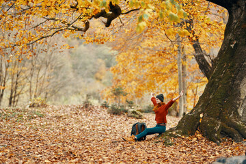 woman with a backpack under a tree in the park and falling leaves autumn landscape