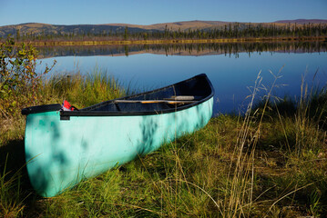 Green Canoe laying on grass on the shore of the lake in sunny morning