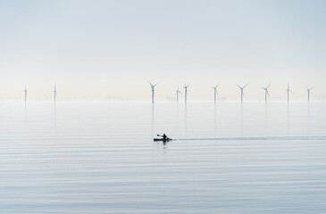 Offshore wind turbines generating electricity off the Essex Clacton coast for an eco backdrop, texture, wallpaper with silhouette kayak in foreground