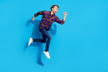 Fototapeta na wymiar Photo of funky hurrying young gentleman dressed checkered shirt smiling jumping running isolated blue color background