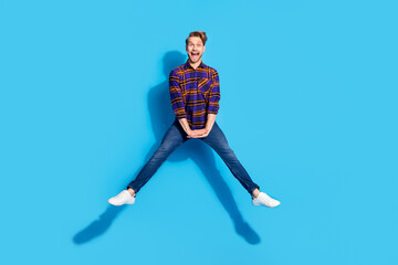 Fototapeta na wymiar Photo of sweet funky young gentleman dressed checkered shirt smiling jumping high isolated blue color background