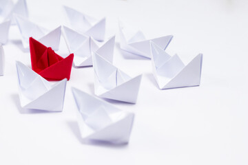 A red paper boat between white boats showing Unique and leadership concept.