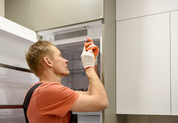 The worker is fixing the built-in refrigerator in the kitchen furniture.