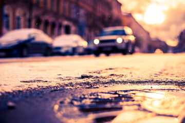 Bright winter sun in a big city, the headlights of the approaching car in the snowfall. Close up view of a hatch at the level of the asphalt