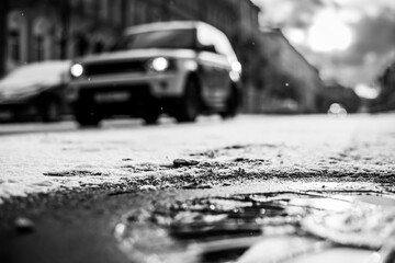 Bright winter sun in a big city, near a passing car in the snowfall. Close up view of a hatch at the level of the asphalt