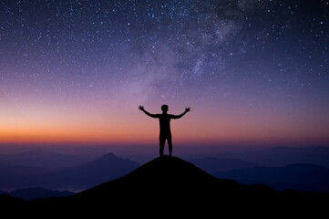Silhouette of young traveler and backpacker watched the star and milky way alone on top of the mountain. He Stand with both hands raised enjoyed traveling and was successful.