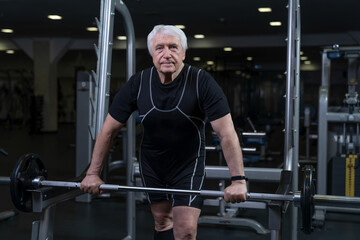 Fototapeta na wymiar an elderly athlete works out in a fitness club with a barbell