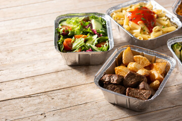 Take away healthy food in foil boxes on wooden table. Copy space