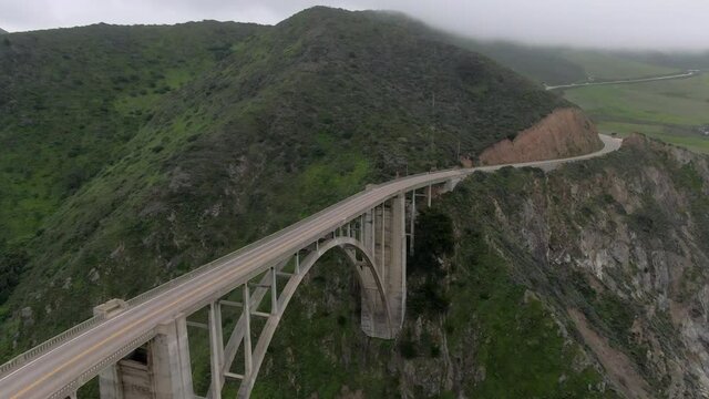 Aerial Shot Of Cars On Famous Bixby Creek Bridge Near Mountains, Drone Flying Forward Over Popular Landmark - Big Sur, California
