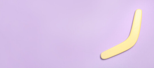 Yellow wooden boomerang on lilac background, top view. Space for text