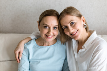 Two adult women are sitting on the couch embracing and looking at the camera.