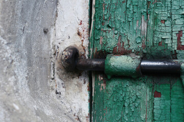 Metal lock on an old wooden door with peeling paint next to a clay wall