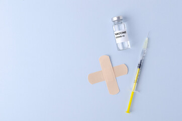 Top view of yellow syringe, glass bottle of vaccine and two beige medical plasters on the bright blue lab table.Empty space