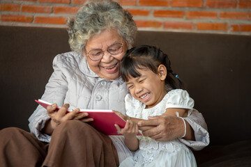 Happy Asia grandmother reading to granddaughter child book at home,Grandmother teaches to read a...