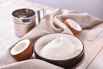 bowl of coconut flour on the table with linen napkin flour sieve and coconut halves