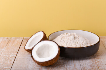 coconut flour in a ceramic bowl on a white wooden table with coconut halves with copy space