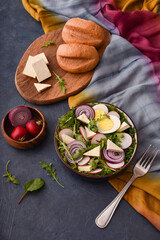 fresh vegetable and egg salad with cheese in brown bowl on blue stone table with colorful napkin and bread on wooden board from top view
