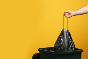 Man throwing garbage bag into bin on yellow background, closeup. Space for text