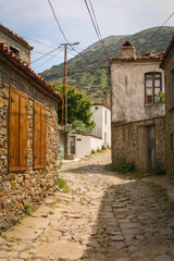 Beautiful old street paved with stones, turkish traditional village houses on both sides, green mountains in the background - Bademli koyu - Gokceada - Canakkale, Turkey